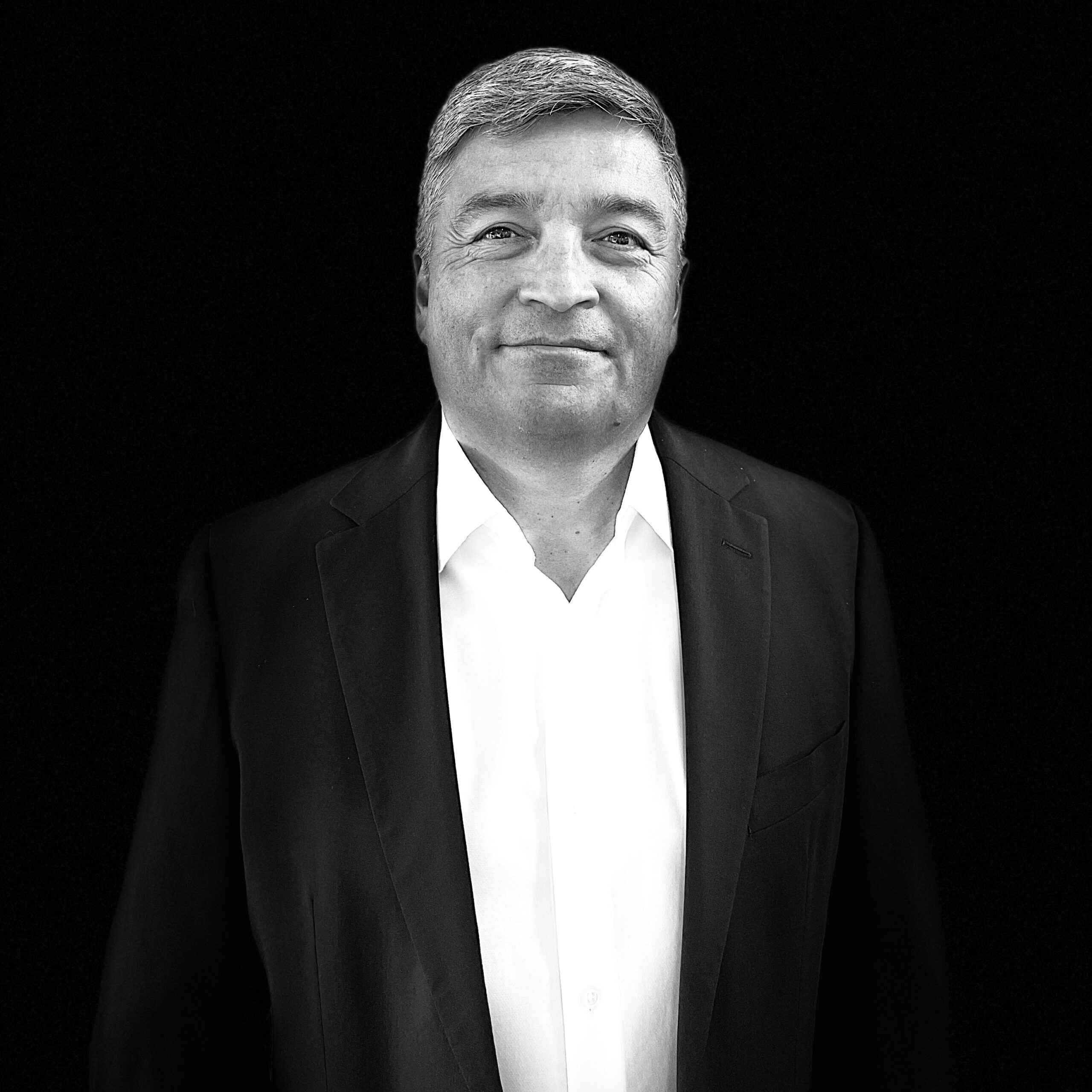 A man in a suit and tie standing up against a black background.